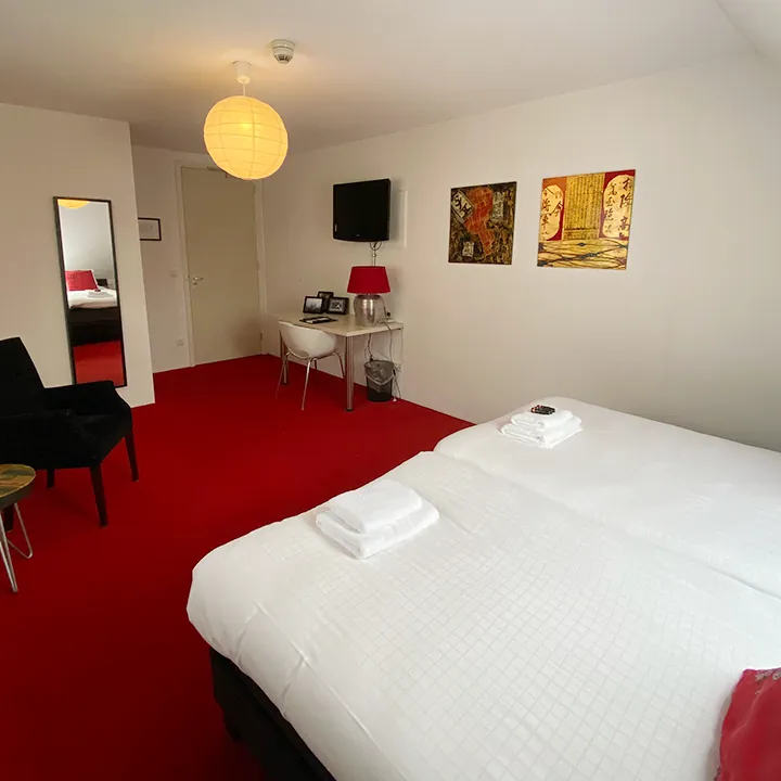 Een kamer met rood tapijt, een warme hanglamp en een donkere fauteuil.