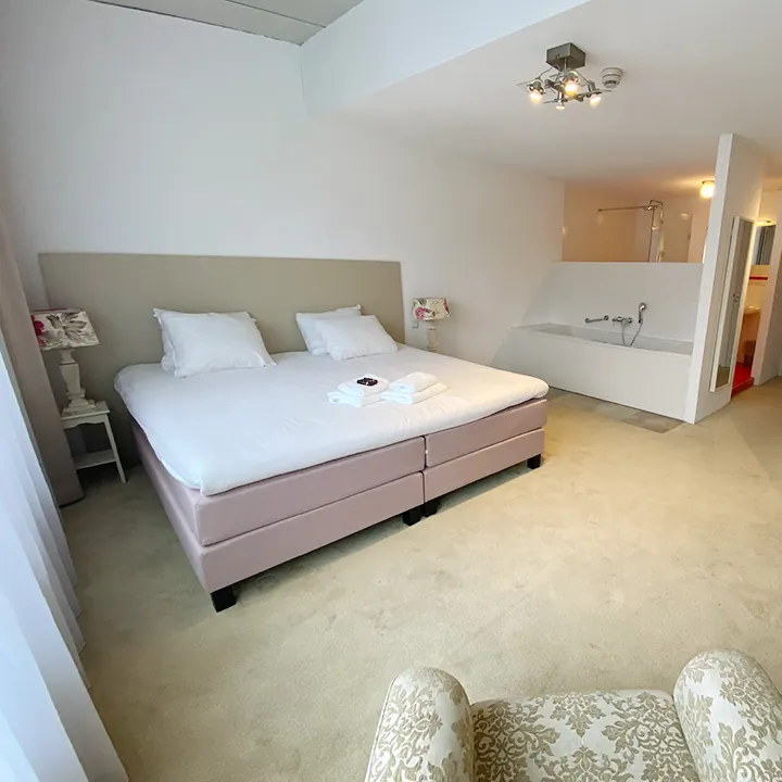 Een crèmekleurige kamer met een gebloemde fauteuil en een bad aan de rechterkant.