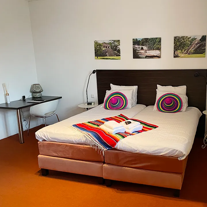 Een bed met terracotta onderstel, een gestreepte deken en ronde geborduurde kussens.
