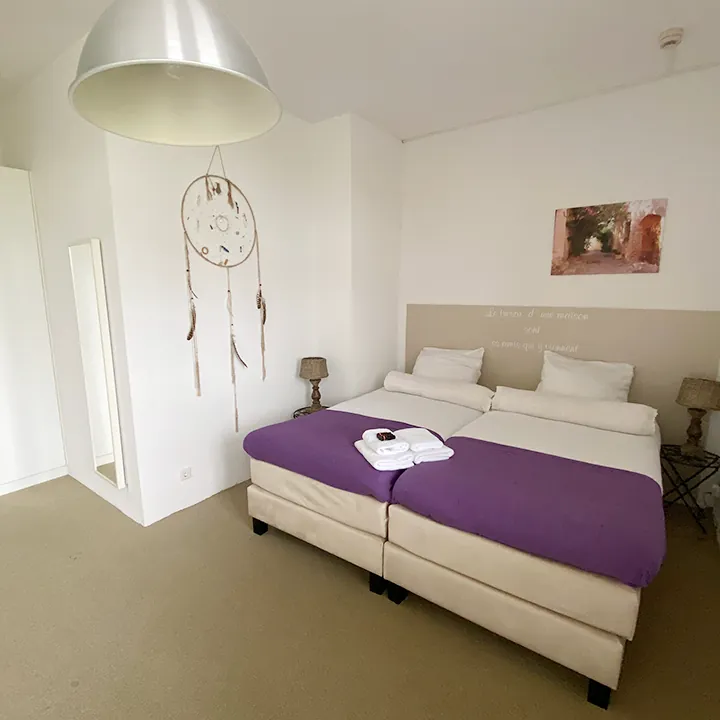 Een dromenvanger aan de wand, een paarse loper over het bed en een grote koepelvormige lamp.