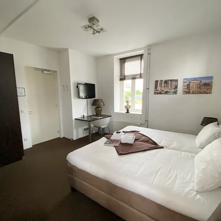 Een kamer met donker tapijt, twee canvasprints van Rome en een bruine plaid.