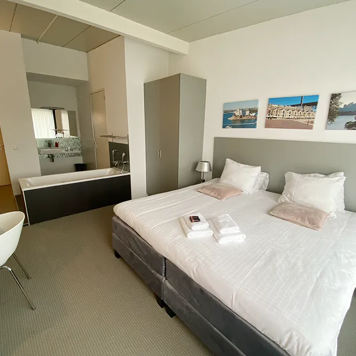 Drie canvasprints van de haven van Sydney boven het bed, met een bad in de kamer.