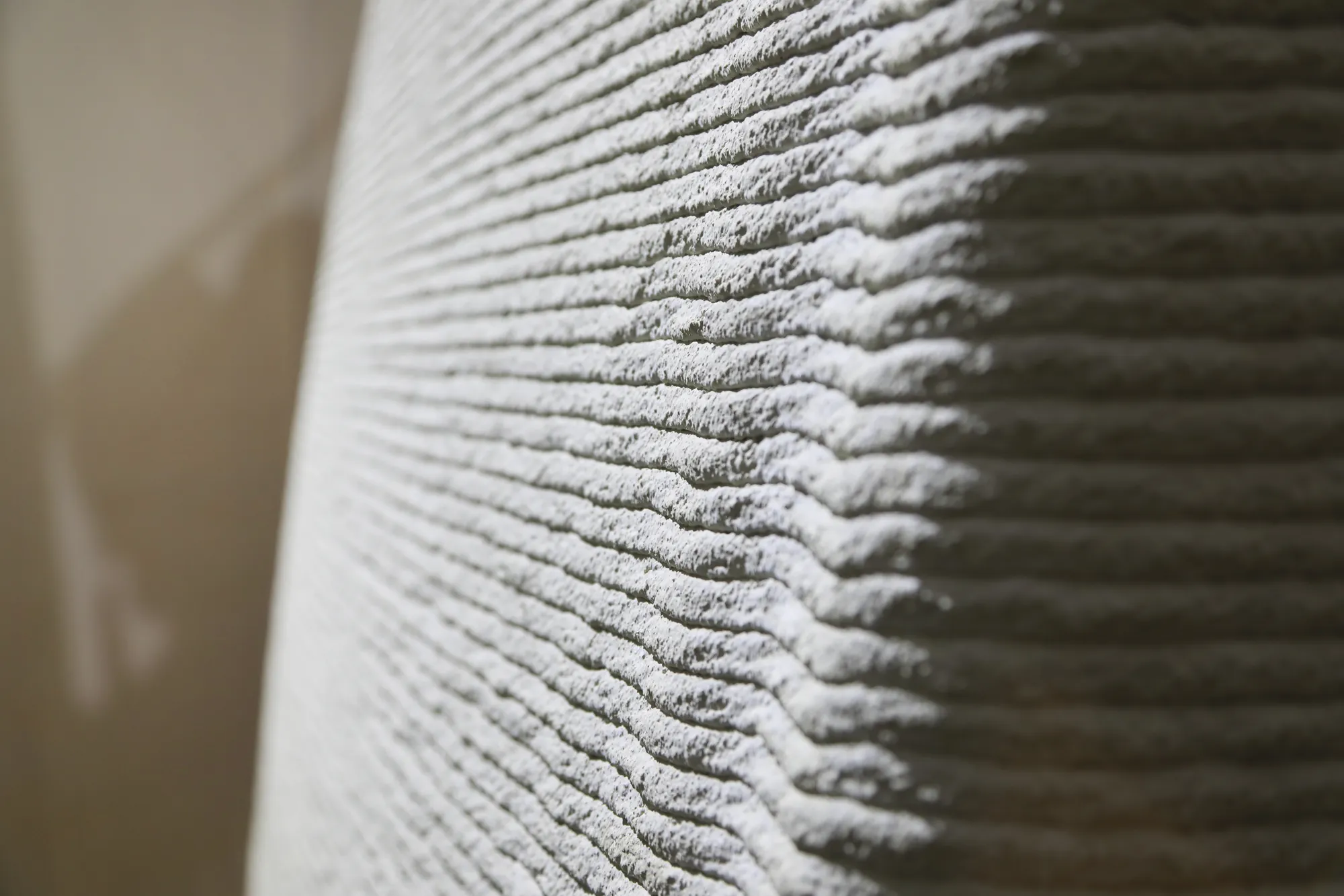 De geprinte betonlagen van dichtbij: horizontale ribbels die met de wand mee buigen.